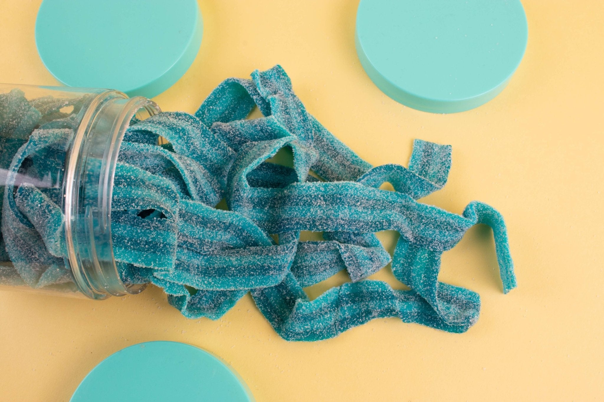 Blue gummy worms spilling out of a jar on a yellow background