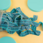 Blue gummy worms spilling out of a jar on a yellow background