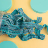 Blue gummy worms spilling out of a jar on a yellow background