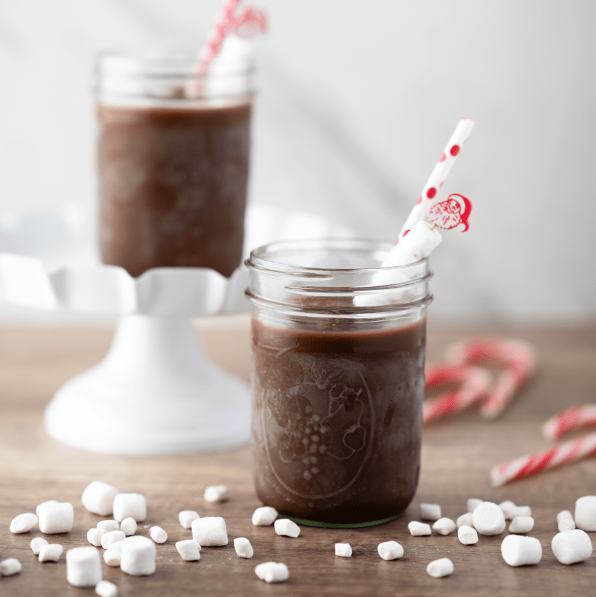 Boozy Frozen Hot Cocoa slush mix pouch with glass of frozen cocoa by fireplace and Christmas tree.