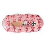 Pink ceramic tray with red bow pattern and wooden spreader featuring peppermint-style handle.