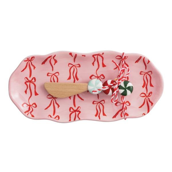 Pink ceramic tray with red bow pattern and wooden spreader featuring peppermint-style handle.