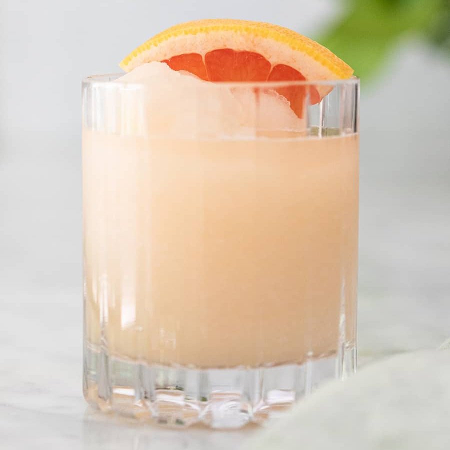 Glass of pink drink with a grapefruit slice on a light background