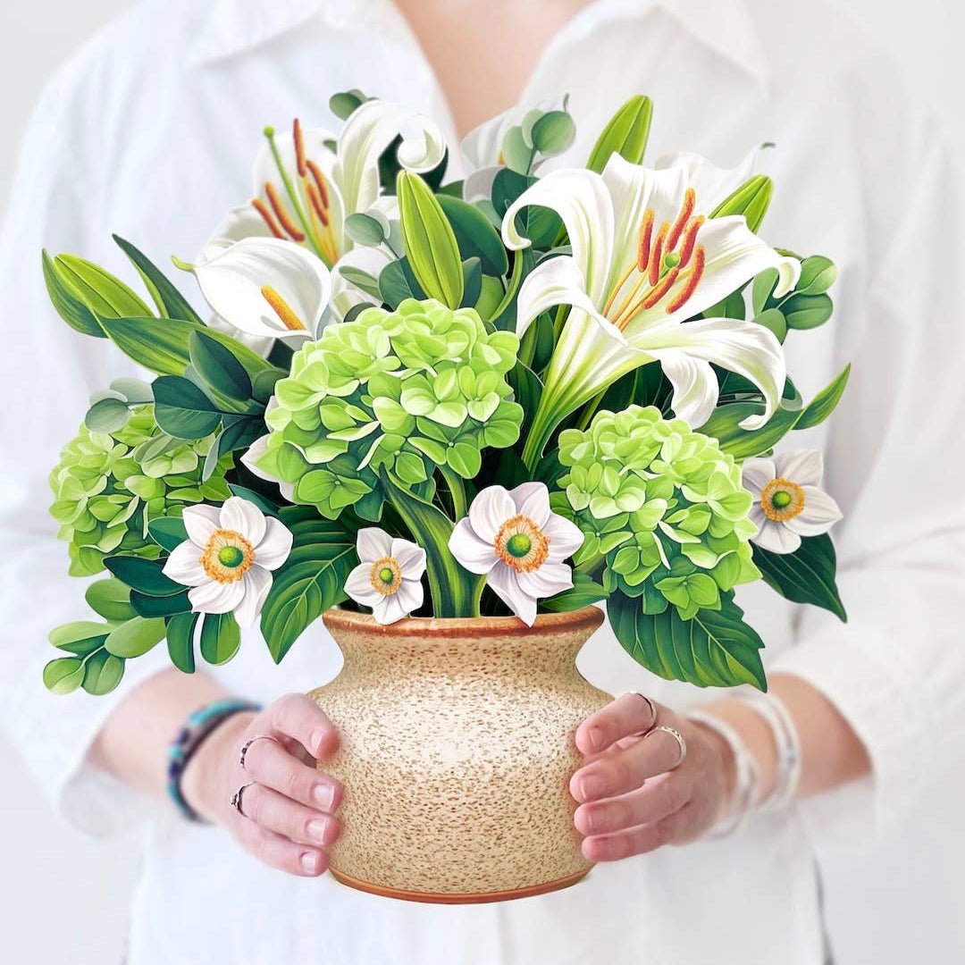 Woman holding a pop-up bouquet of ivory lilies, green hydrangeas, and eucalyptus in a stone-textured vase