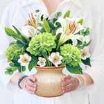 Woman holding a pop-up bouquet of ivory lilies, green hydrangeas, and eucalyptus in a stone-textured vase