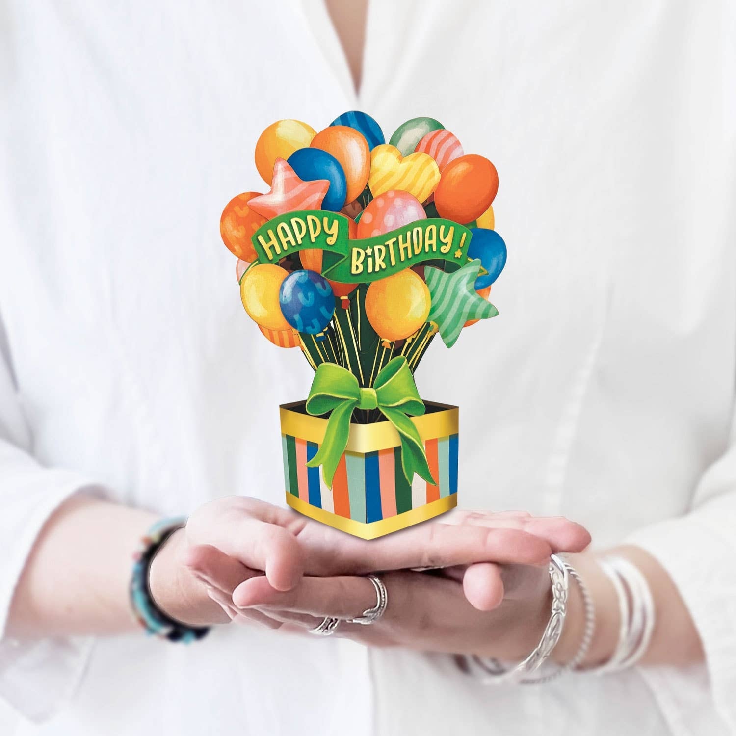 Hands holding a mini pop-up card with colorful balloons emerging from a striped gift box