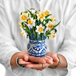 Hands holding a mini pop-up bouquet of daffodils and grape hyacinths in a blue and white vase
