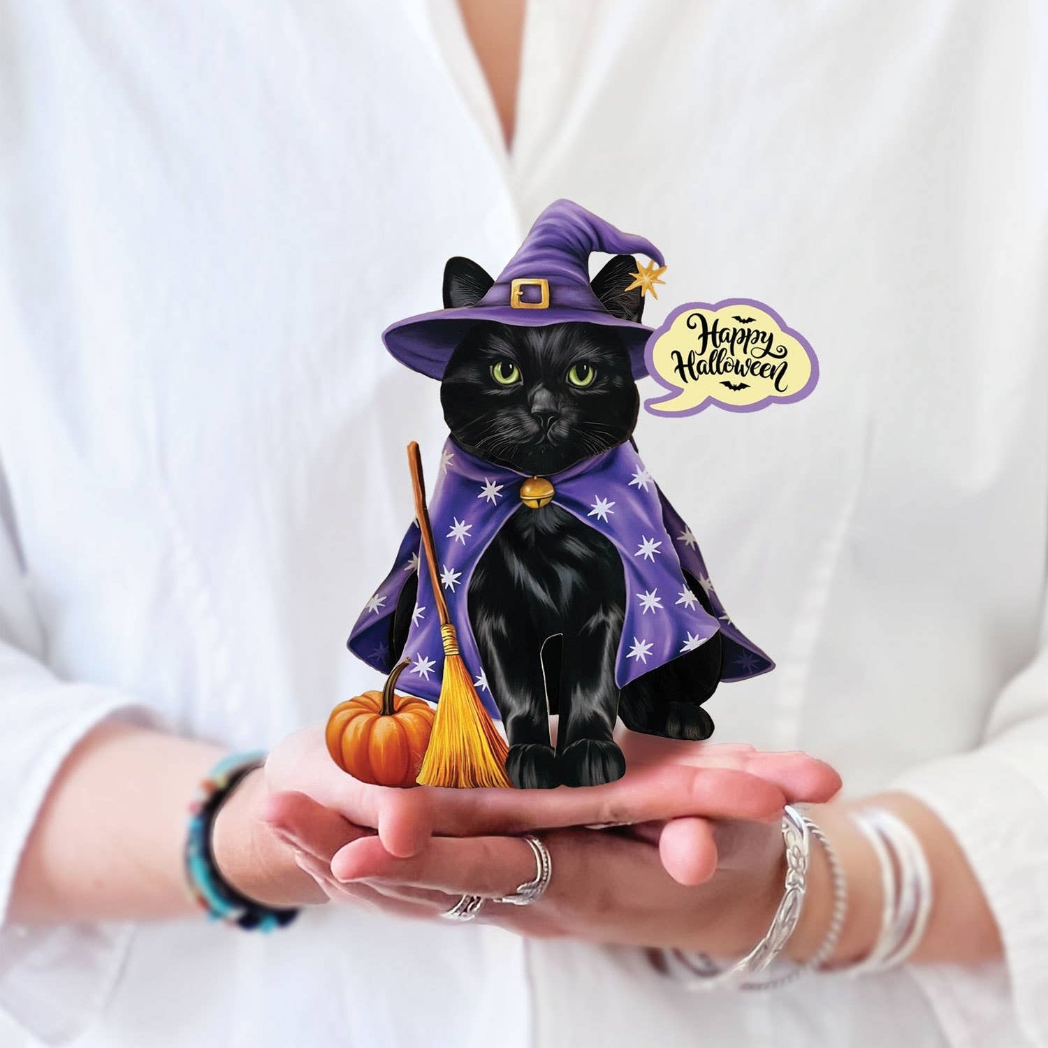 Hands holding a mini Halloween pop-up card featuring a black cat in a purple witch costume with a pumpkin and broom