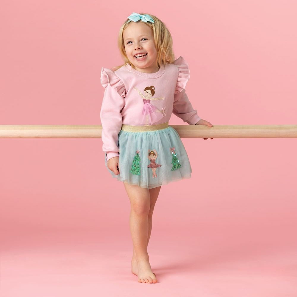 Young girl in a pink sweater and green skirt standing on a pink background