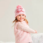 Child wearing a pink coat, hat, and boots standing on a snowy surface.