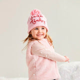 Child wearing a pink coat, hat, and boots standing on a snowy surface.