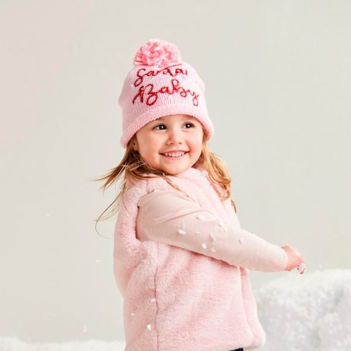 Child wearing a pink coat, hat, and boots standing on a snowy surface.