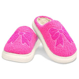 Pair of bright pink chenille slippers with embroidered bow designs and skid-resistant white soles, made for children.