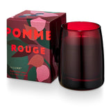 Pomme Rouge candle in deep red glass with bold, colorful packaging featuring fruit and foliage design