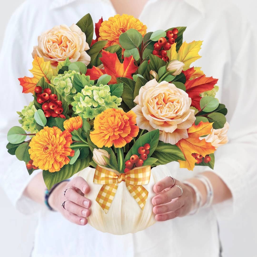 Woman holding a pop-up bouquet of fall flowers in a white pumpkin vase with a gingham bow