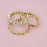 Gold bracelets with colorful gemstones on a pink background