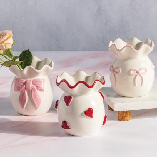 White ceramic bud vase with pink bow and ruffled top edge.