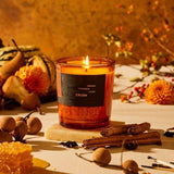Crush candle in amber glass vessel with lit flame, styled with cinnamon sticks and fall florals
