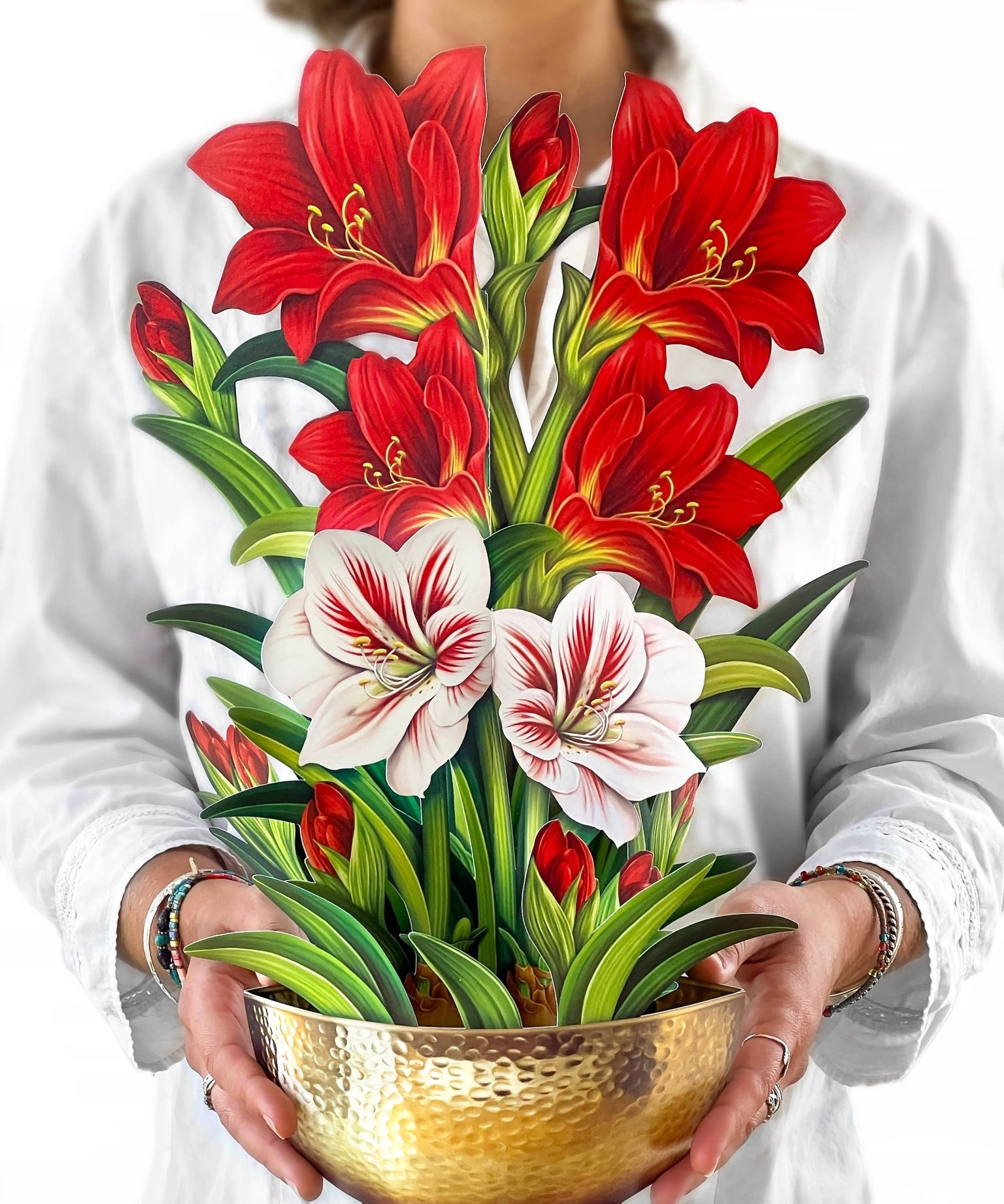 Woman holding a tall pop-up bouquet of red and white amaryllis flowers in a gold hammered bowl