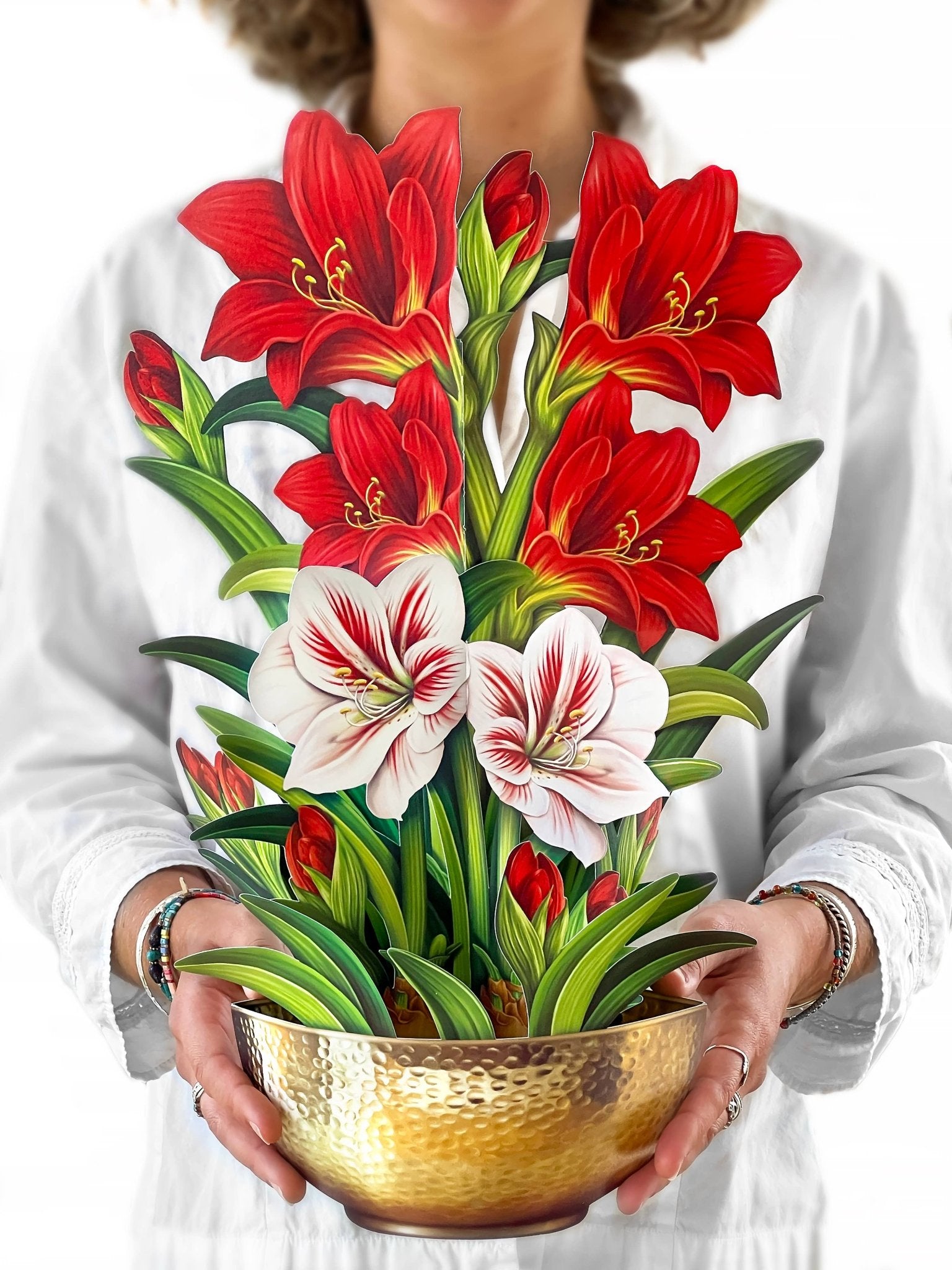 Woman holding a tall pop-up bouquet of red and white amaryllis flowers in a gold hammered bowl