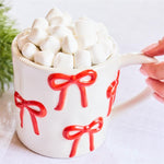 White ceramic mug with raised red bow design by Mary Square, filled with marshmallows.