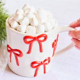 White ceramic mug with raised red bow design by Mary Square, filled with marshmallows.