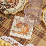 Decorative table setting with plaid tablecloth, glass, and autumn-themed cards.