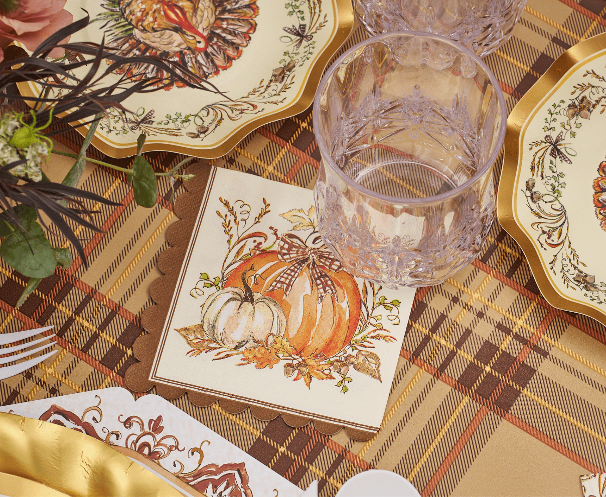 Decorative table setting with plaid tablecloth, glass, and autumn-themed cards.