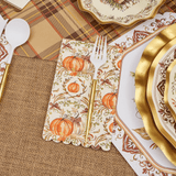 Thanksgiving-themed table setting with gold plates, pumpkins, and burlap placemats.