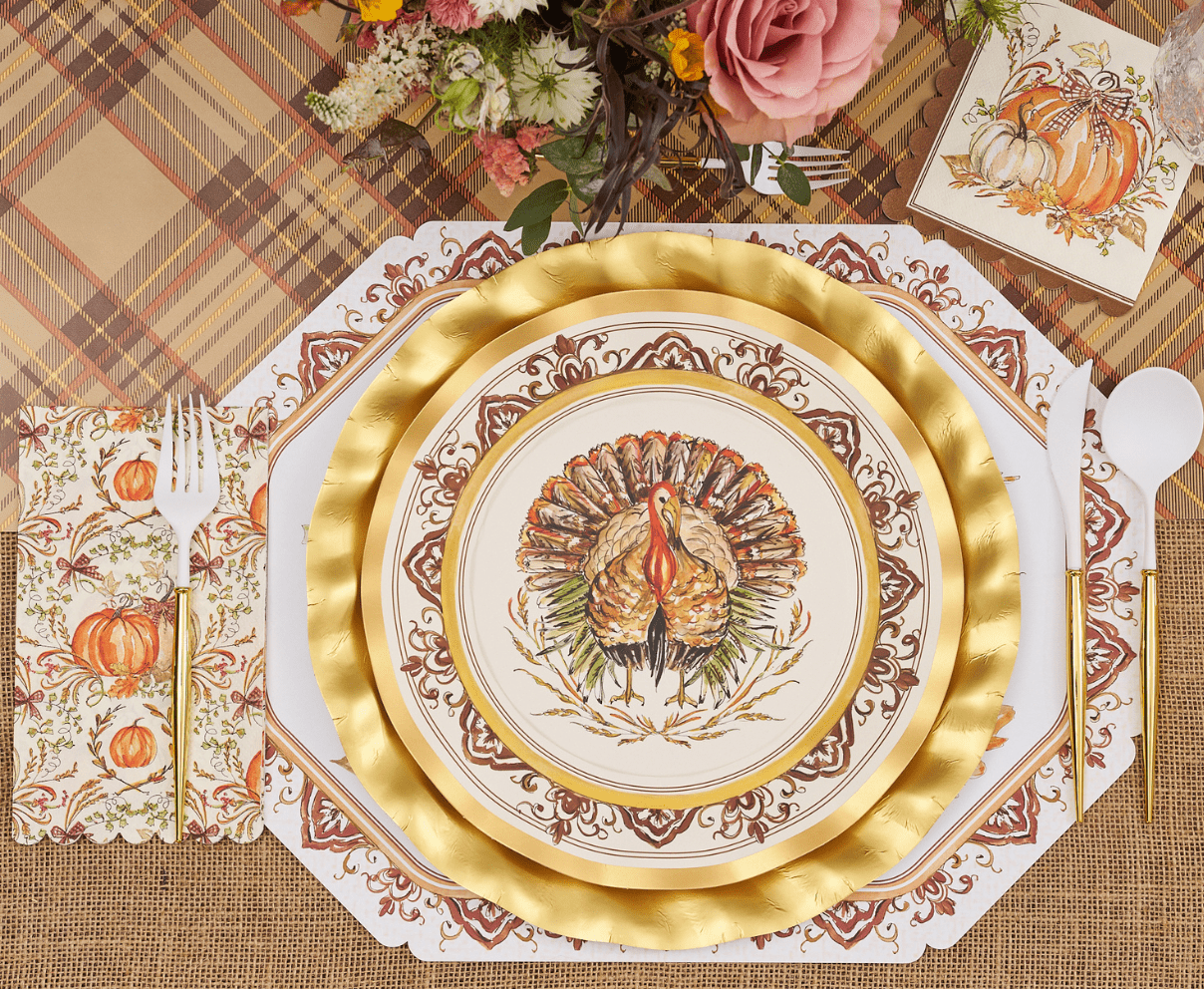 Thanksgiving-themed place setting with gold plates, turkey design, and decorative napkins on a plaid tablecloth.