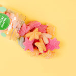 Colorful star-shaped gummy candies spilling out of a transparent container on a yellow background.