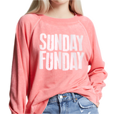 Woman wearing coral graphic sweatshirt with bold white “Sunday Funday” lettering
