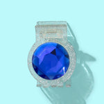 Clear claw clip with silver glitter and round blue gemstone on each side, styled on blue background