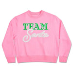 Pink Team Santa sweatshirt with green and white glitter lettering, made of soft polyester, cotton, and rayon blend, available in children’s sizes.