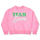 Pink Team Santa sweatshirt with green and white glitter lettering, made of soft polyester, cotton, and rayon blend, available in children’s sizes.
