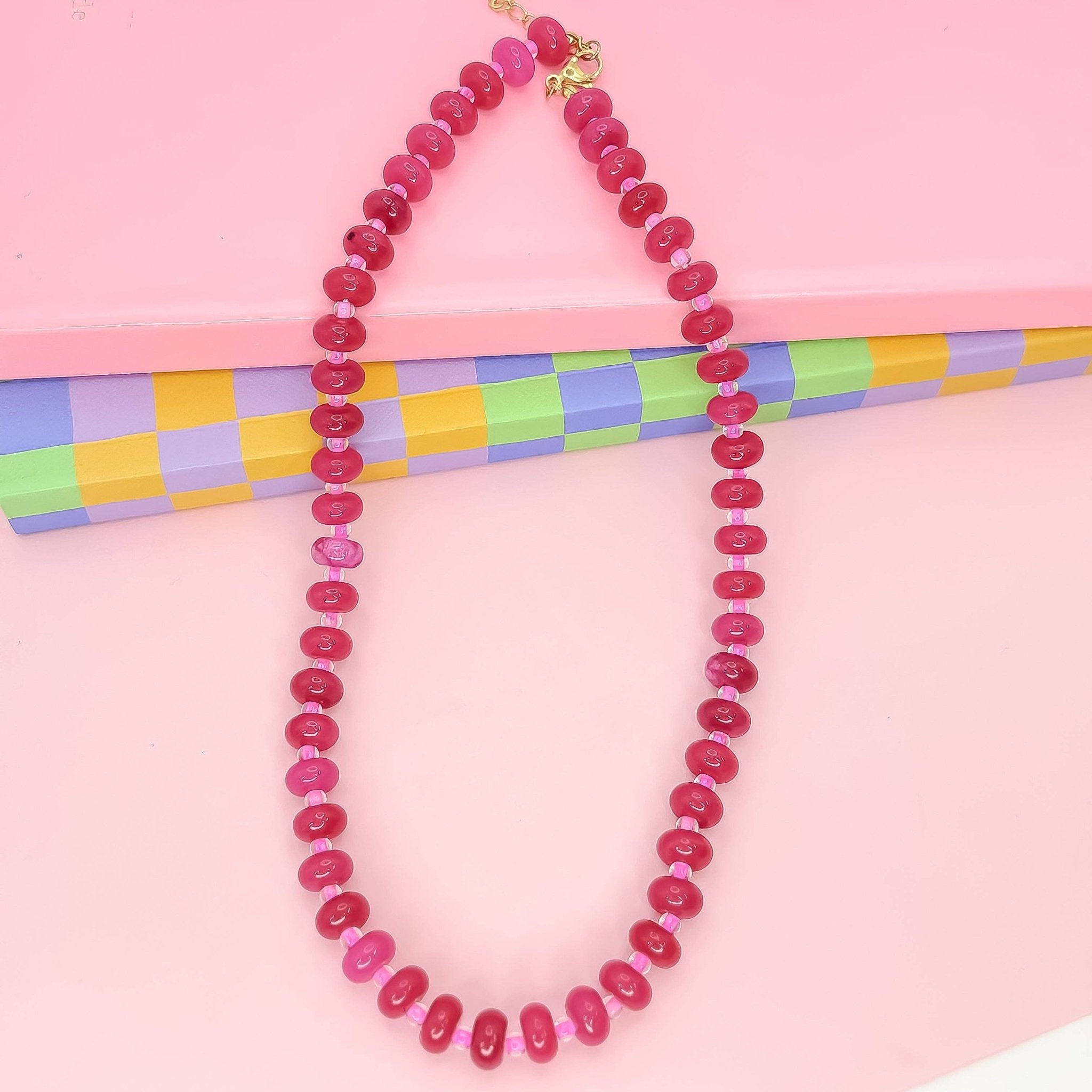Pink beaded necklace on a pink background with colorful paper