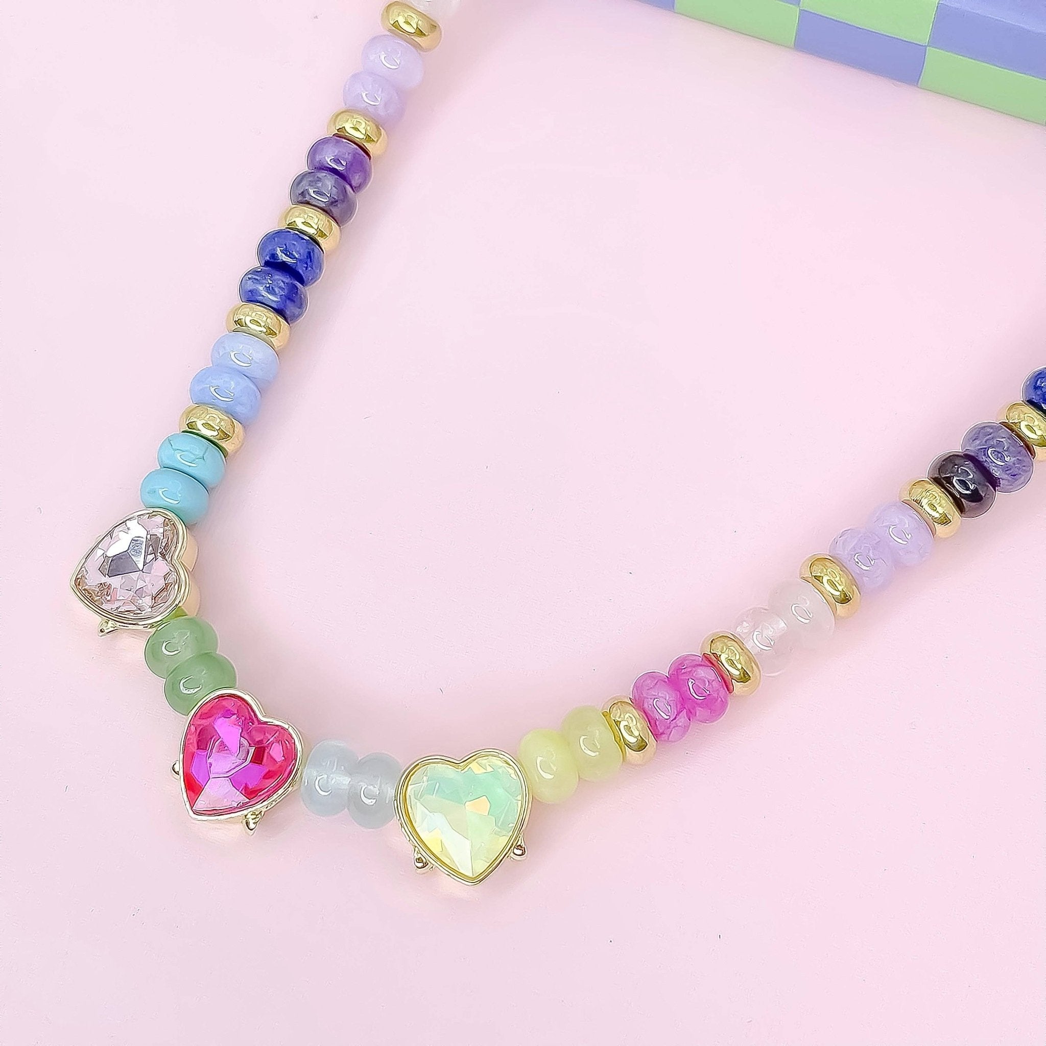 Colorful beaded necklace with heart-shaped gemstones on a pink background