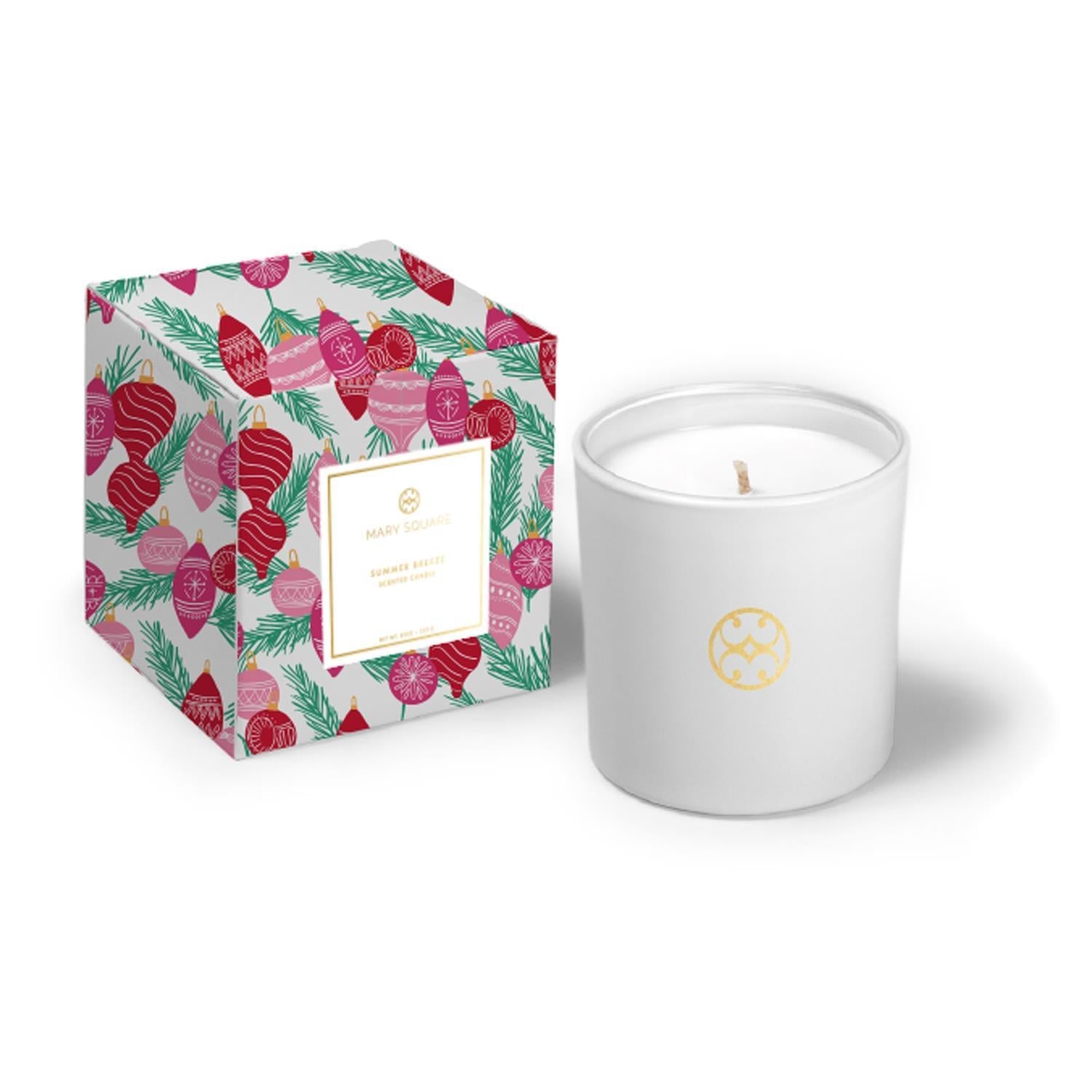 White candle with gold logo next to a decorative box with Christmas design on a white background