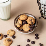 Cookies with chocolate chips in a bowl on a beige surface with a glass of milk.